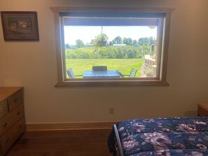 A bedroom with a window overlooking a grassy area and a table. - Welcome to Selah Hills Ranch – a Tranquil, Digital Detox Off-Grid Haven (Agency)
