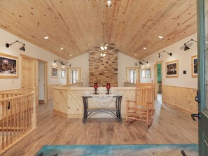 A spacious room with a high wooden ceiling, a central stone fireplace, and a large wooden dining table with chairs. - Welcome to Selah Hills Ranch – a Tranquil, Digital Detox Off-Grid Haven (Agency)