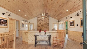 A spacious room with a high wooden ceiling, a central stone fireplace, and a large wooden dining table with chairs. - Main Selah Hills Ranch (Agency)