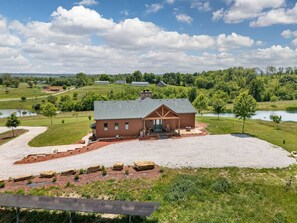 A rustic barn-style building with a gravel driveway and a pond in the background. - Welcome to Selah Hills Ranch – a Tranquil, Digital Detox Off-Grid Haven (Agency)