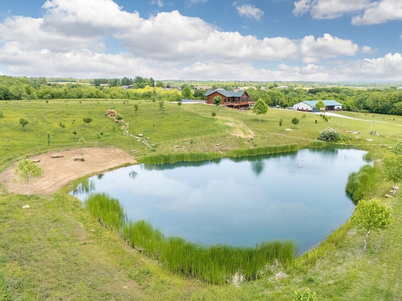 Un grand étang entouré de champs verdoyants, avec une ferme et d’autres bâtiments en arrière-plan.