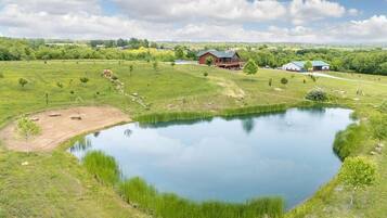 Un grand étang entouré de champs verdoyants, avec une ferme et d’autres bâtiments en arrière-plan.
