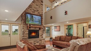 A spacious living room with a stone fireplace, leather sofas, and a large flat-screen TV. - Main Selah Hills Ranch (Agency)