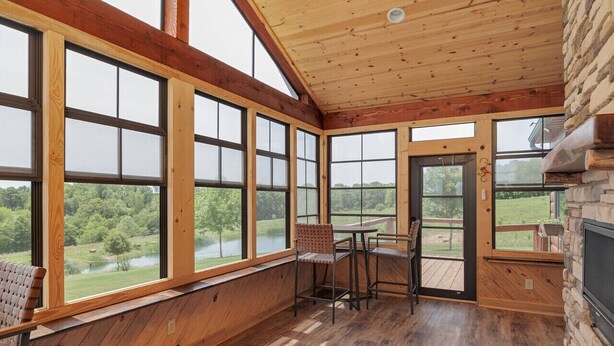 A spacious room with large windows, a wooden ceiling, and a stone fireplace. - Main Selah Hills Ranch (Agency)