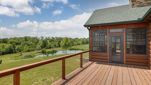 A wooden cabin with a deck overlooking a lake and forest. - Main Selah Hills Ranch (Agency)