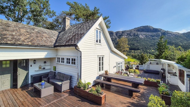 A white house with a sloped roof, a deck with outdoor furniture, and a mountain view in the background.