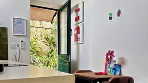 A hotel room with a wooden reception desk, a small table with a chair, a window with a view of greenery, and a wall-mounted air conditioner. - Carioquinha Studio - Aveiro city center (Aveiro)