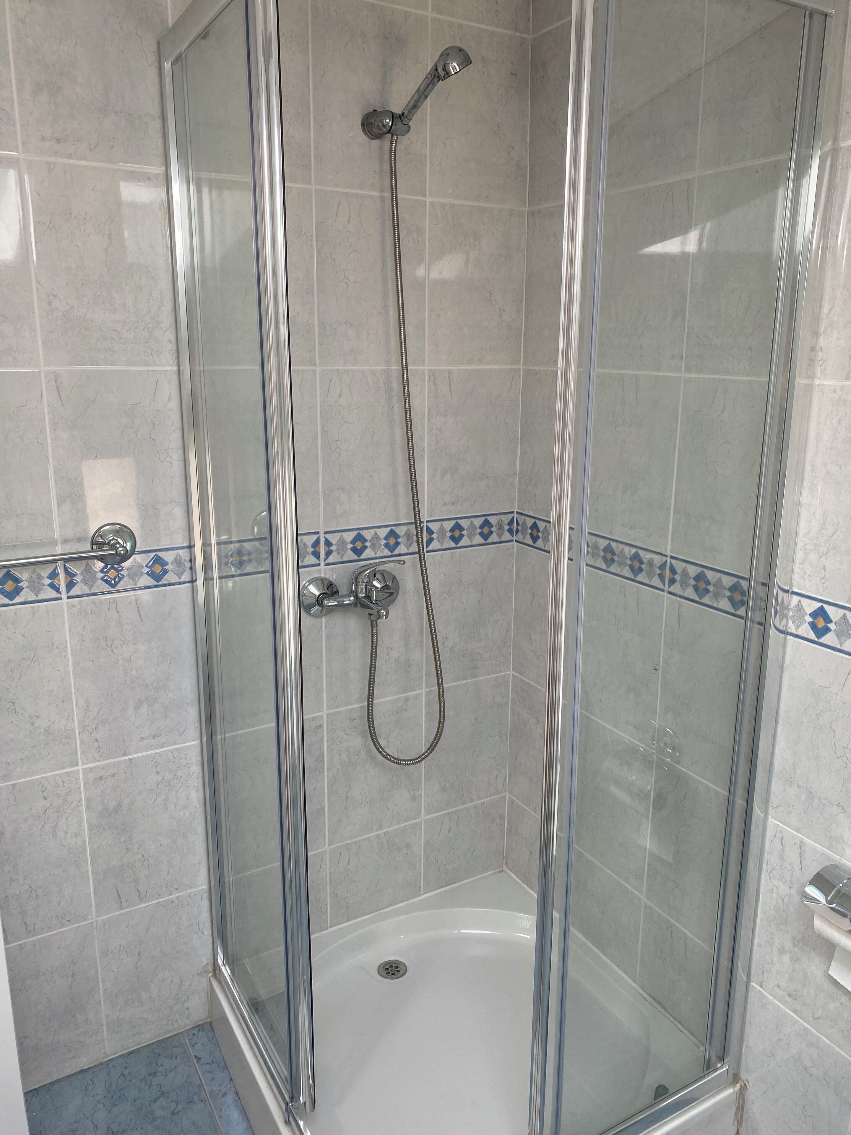 A glass-enclosed shower stall with a handheld showerhead and a wall-mounted faucet.