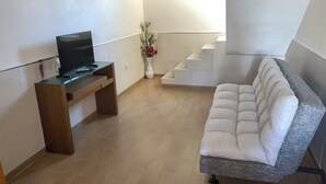 Un salon moderne avec un téléviseur à écran plat posé sur un meuble en bois, un canapé gris et un escalier menant à un niveau supérieur.