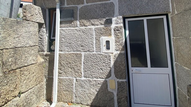 Un bâtiment en pierre avec un toit recouvert de tuiles, une porte et une cheminée.