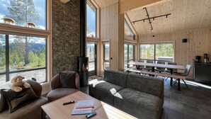 A spacious living area with a stone wall, large windows, a fireplace, and a dining area with a table and chairs. - Awesome home in Gålå with sauna (Gålå)