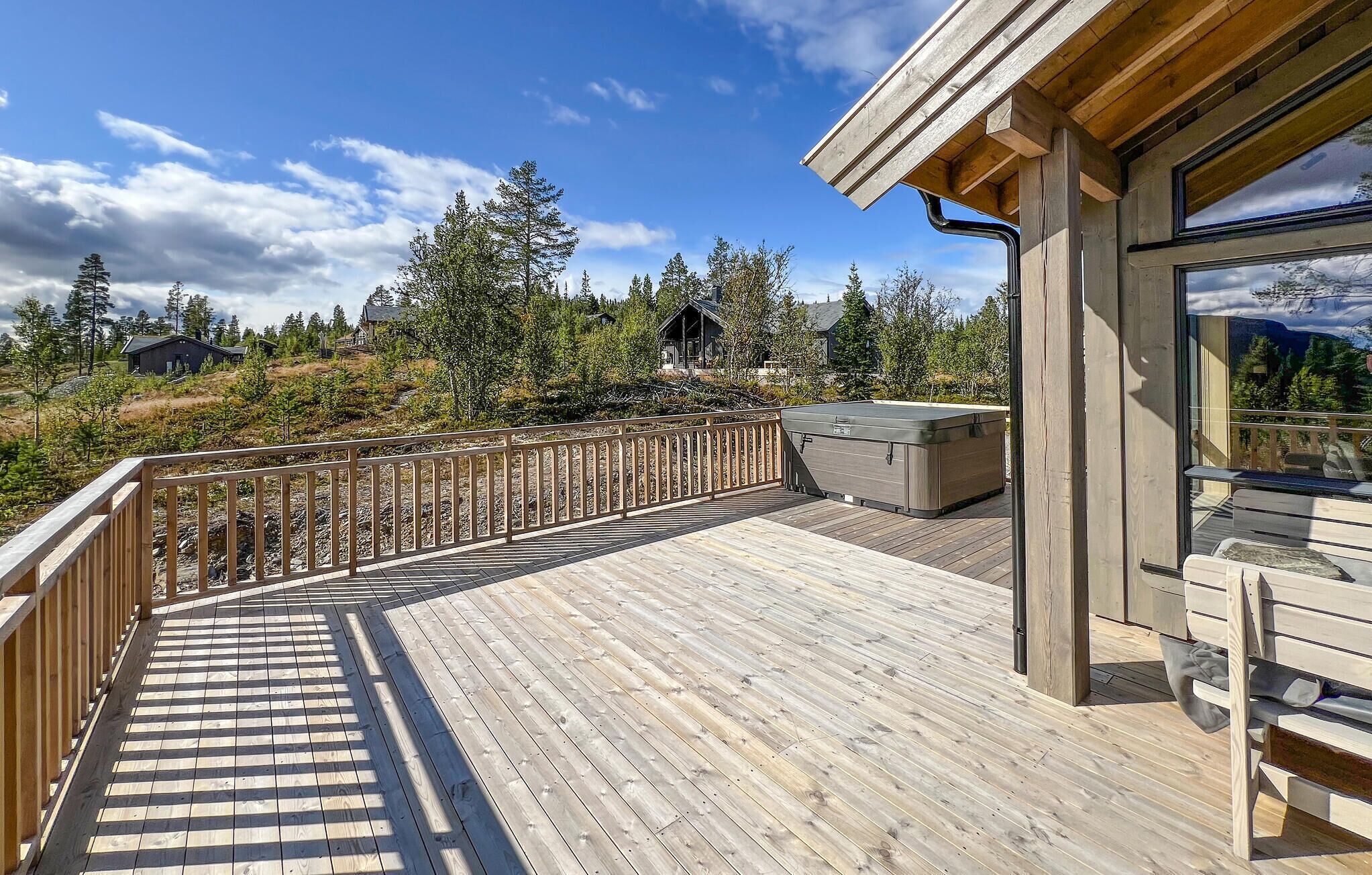 A wooden deck with a view of a mountain landscape, a hot tub, and a cabin in the background.