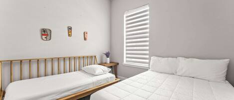 A bedroom with two beds, a wooden headboard, a small bedside table with a vase, and a window with blinds.