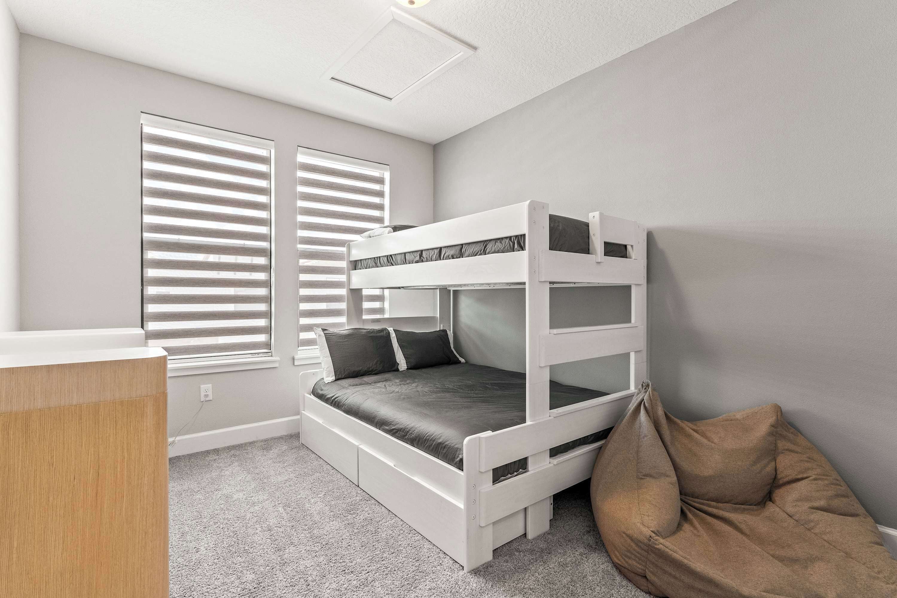 A bunk bed with a desk and storage drawers, a bean bag chair, and a window with blinds.