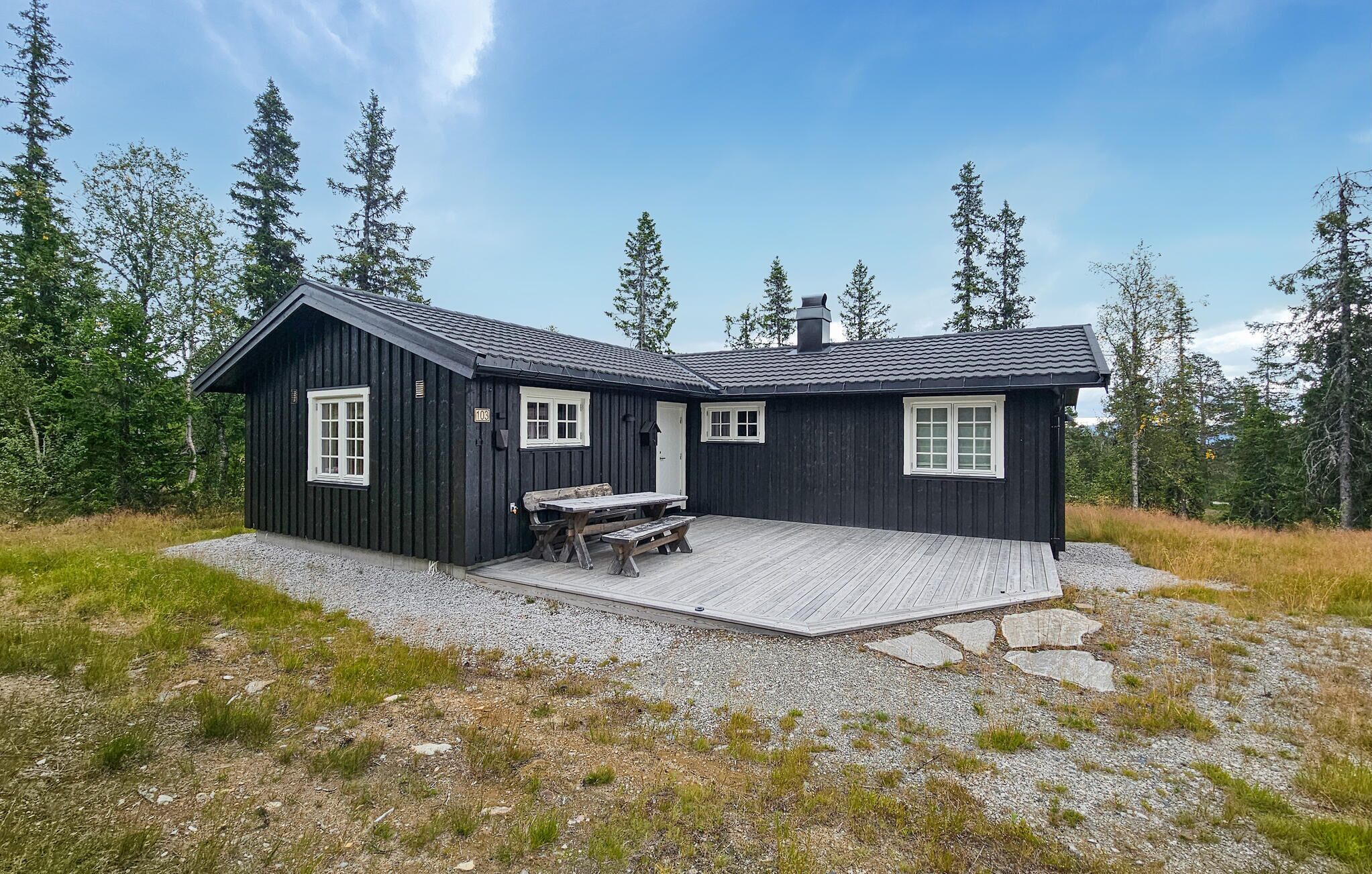 A black wooden cabin with two windows, a porch, and a table.