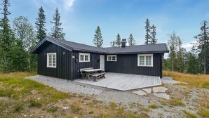 Une cabane en bois noire, dotée de deux fenêtres, d’un porche et d’une table.