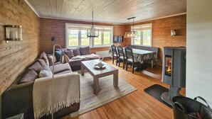 Un salon chaleureux avec un décor intérieur en bois, un ensemble de canapés, une table à manger avec des chaises et une cheminée.