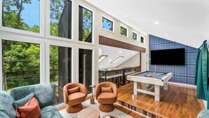 Una sala de estar moderna con mesa de billar, asientos cómodos y ventanas amplias con vistas al exterior.