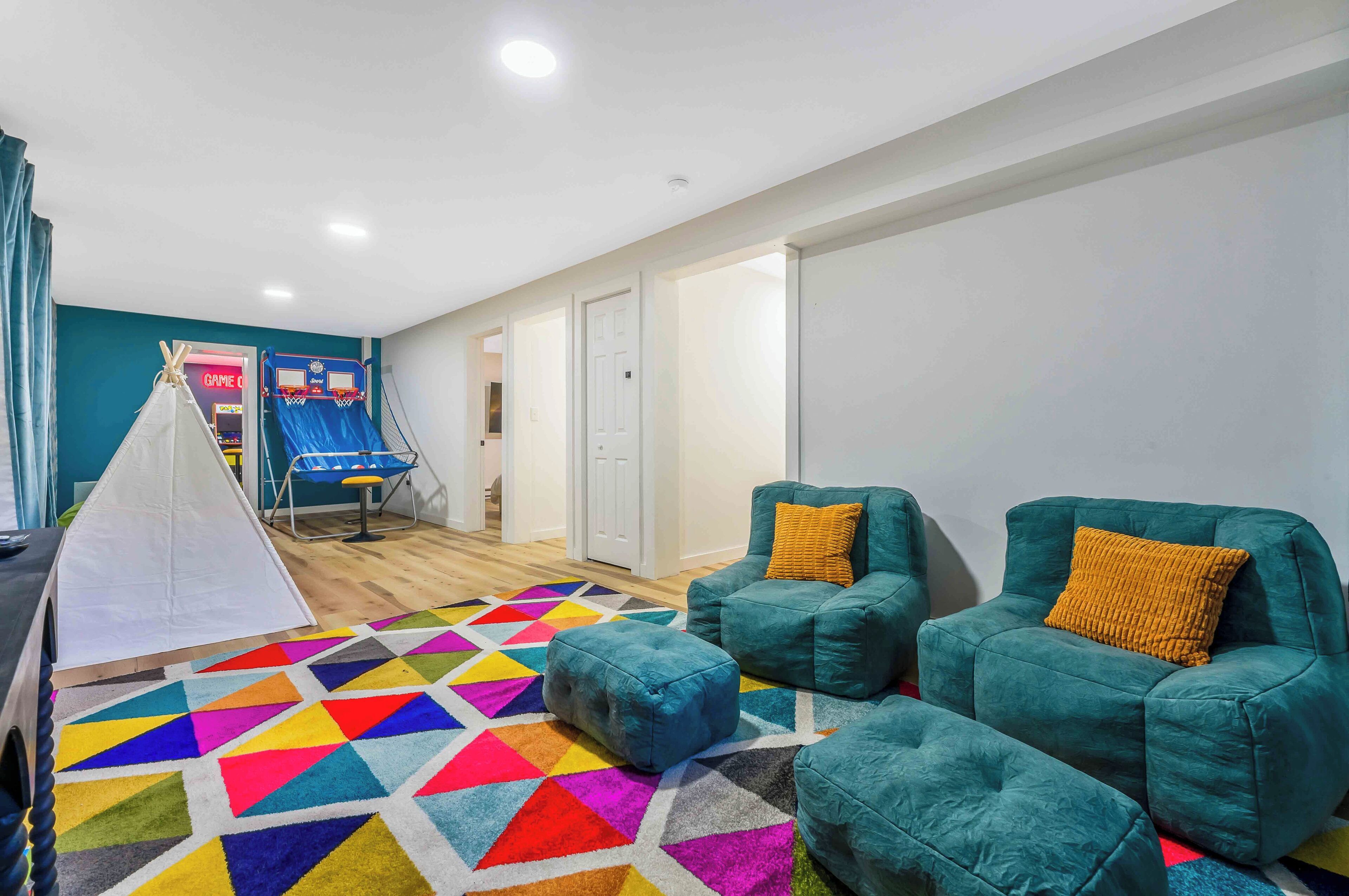 Una habitación con sillones color turquesa, un tapete geométrico de colores, una carpa blanca y un aro de baloncesto.