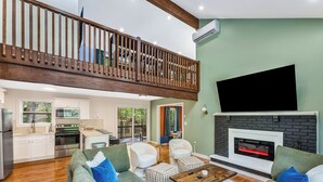 Amplia sala de estar con techo alto, chimenea, televisor y balcón.