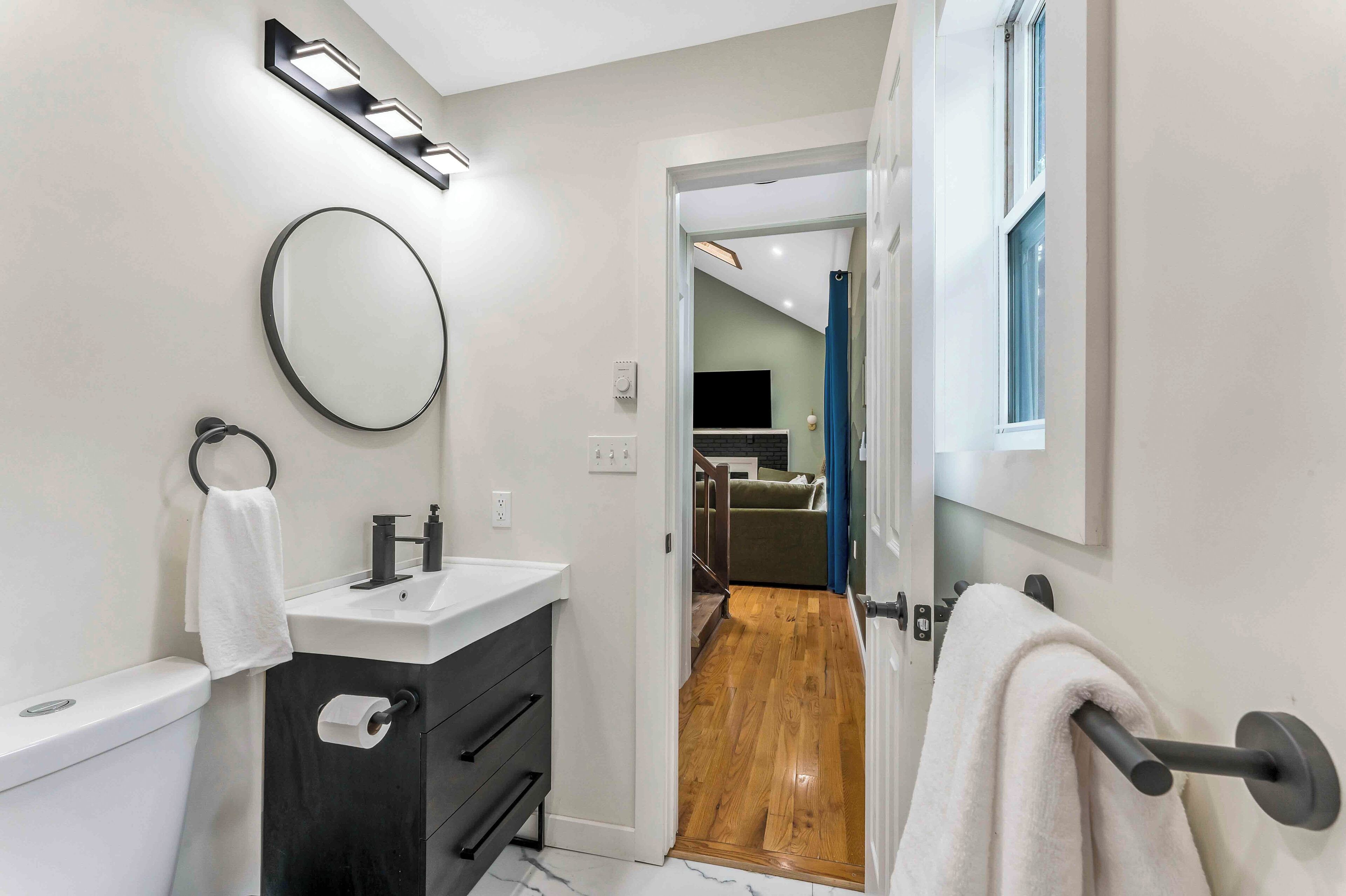 A modern bathroom with a toilet, sink, and mirror. There is a towel rack with a towel hanging on it. The bathroom has a wooden floor and a door leading to another room.