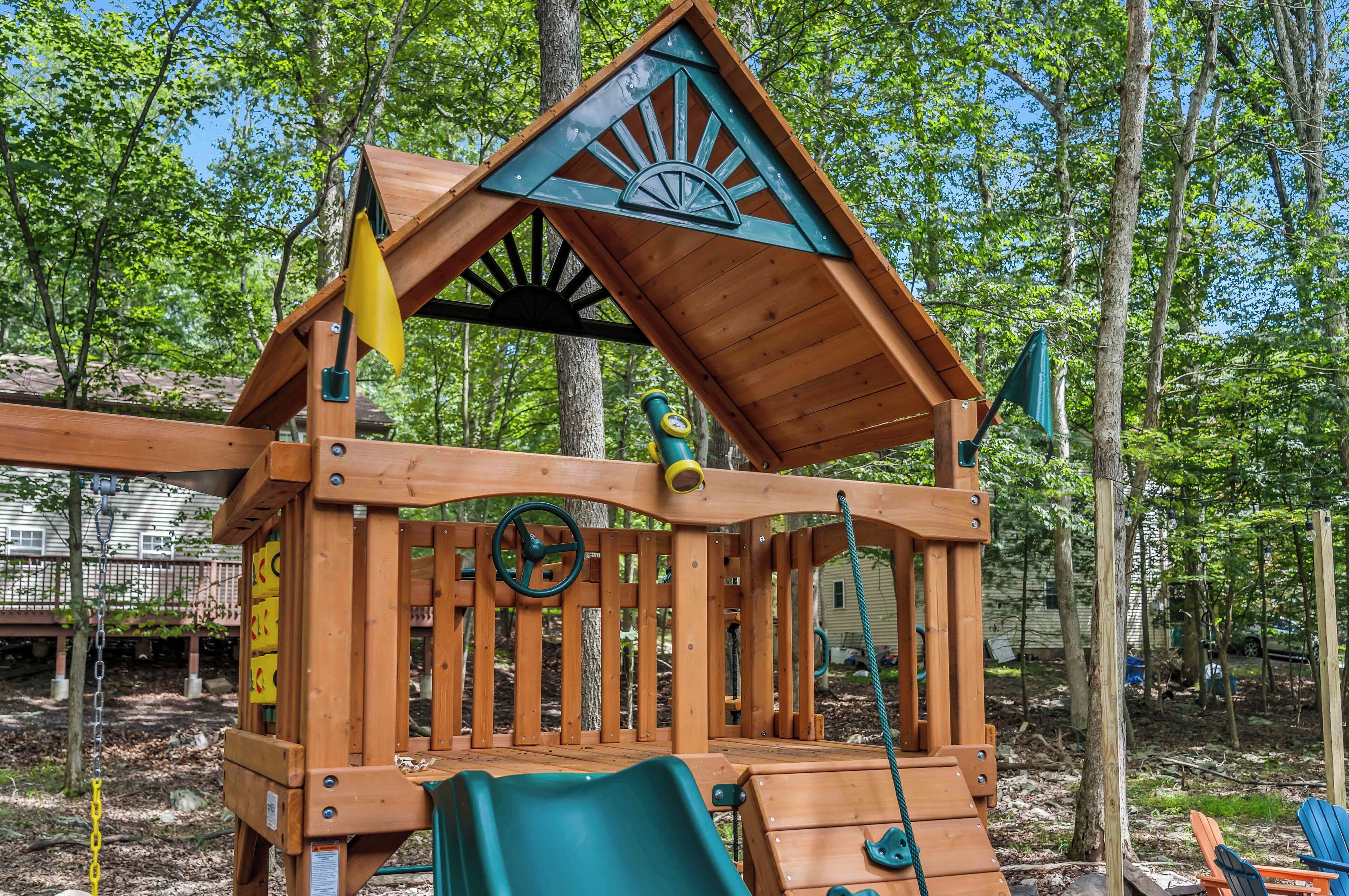 A wooden play structure with a roof, slides, and climbing elements, surrounded by trees.