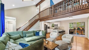 Un salón espacioso con un sofá verde, una mesa de centro de madera y una escalera que sube a un nivel superior.