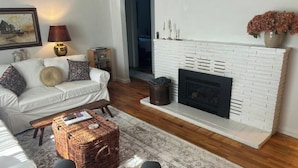A living room with a white sofa, a fireplace, and a rug. - Charming Lovely 1940s Bungalow (Ashland)