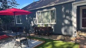 A house with a number 706 on the side, a red umbrella, a patio with a patterned rug, and a small garden area. - Charming Lovely 1940s Bungalow (Ashland)