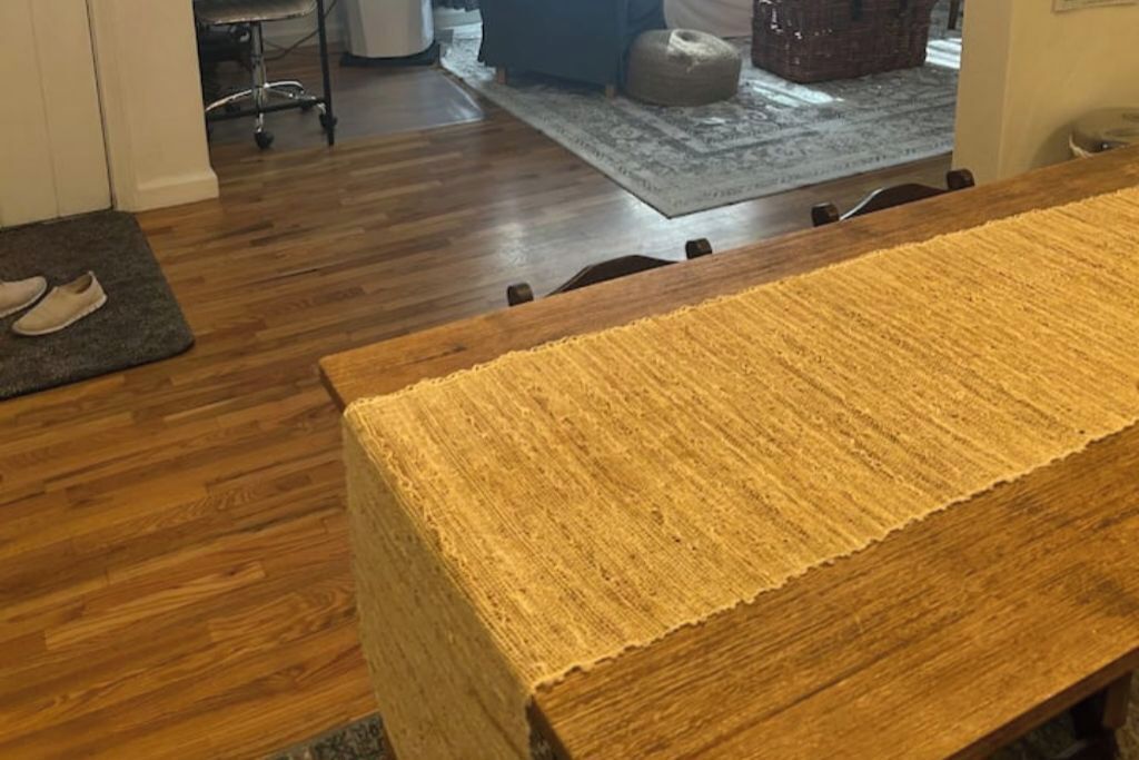 Ein Holztisch mit strukturierter Tischläufer, ein grauer Teppich und ein Paar Hausschuhe auf einer Fußmatte.