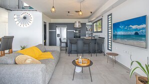 A modern living room with a grey sofa, yellow throw, and a dining area with bar stools.