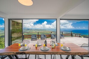 Mesa de comedor lista para cuatro personas con vista panorámica al océano, sillas exteriores y una terraza de madera.