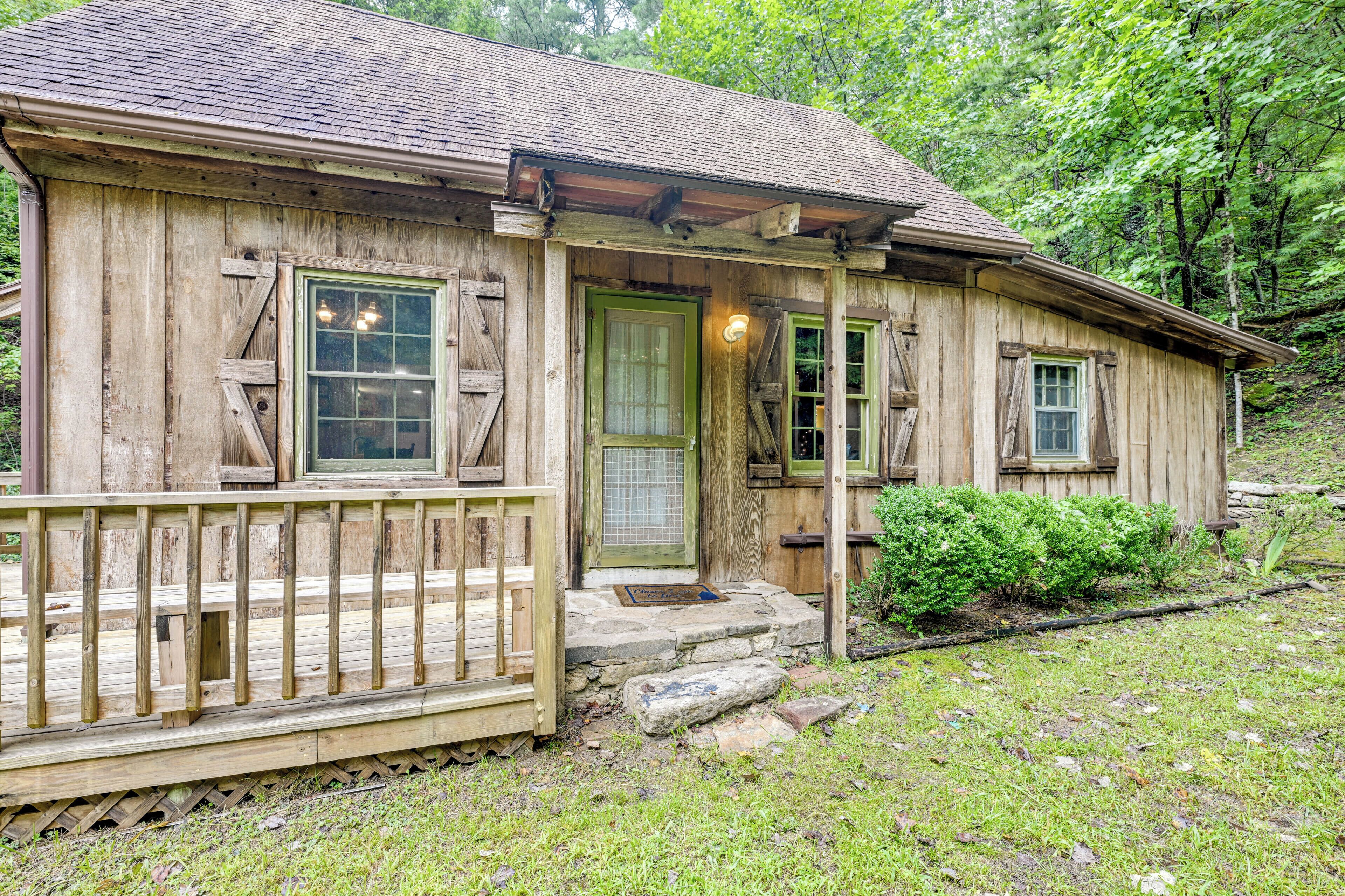 A rustic wooden cabin with a porch, a stone entrance, and a small garden area.