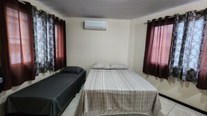 Une chambre avec deux lits simples, une petite table et un appareil de climatisation fixé au mur.