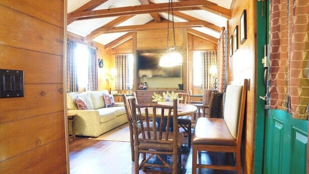 A cozy wooden interior with a dining table and chairs, a sofa, and a kitchen area.