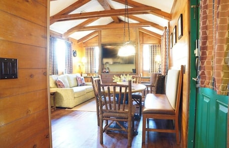 A cozy wooden interior with a dining table and chairs, a sofa, and a kitchen area.