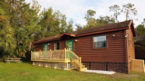 A wooden cabin with a porch, a stone foundation, and a small deck.