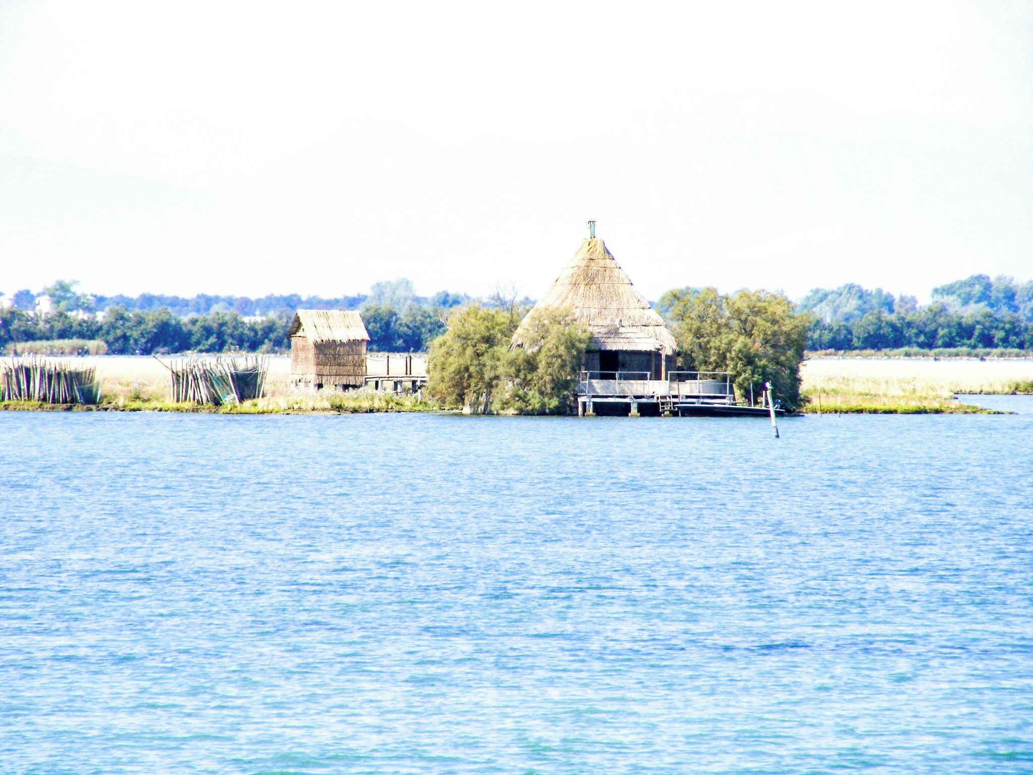 Ein rustikales Haus mit Strohdach und einem Steg, der in ruhiges Wasser führt.