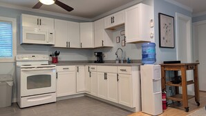 A kitchen with white cabinets, a microwave, stove, and a water dispenser.