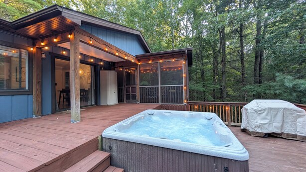 A wooden deck with a hot tub, string lights, and a covered barbecue area.