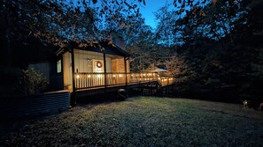 A wooden cabin with a deck, surrounded by trees.