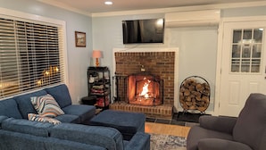 A cozy living room with a fireplace, a television mounted above it, and a comfortable seating area with a sofa and armchair.