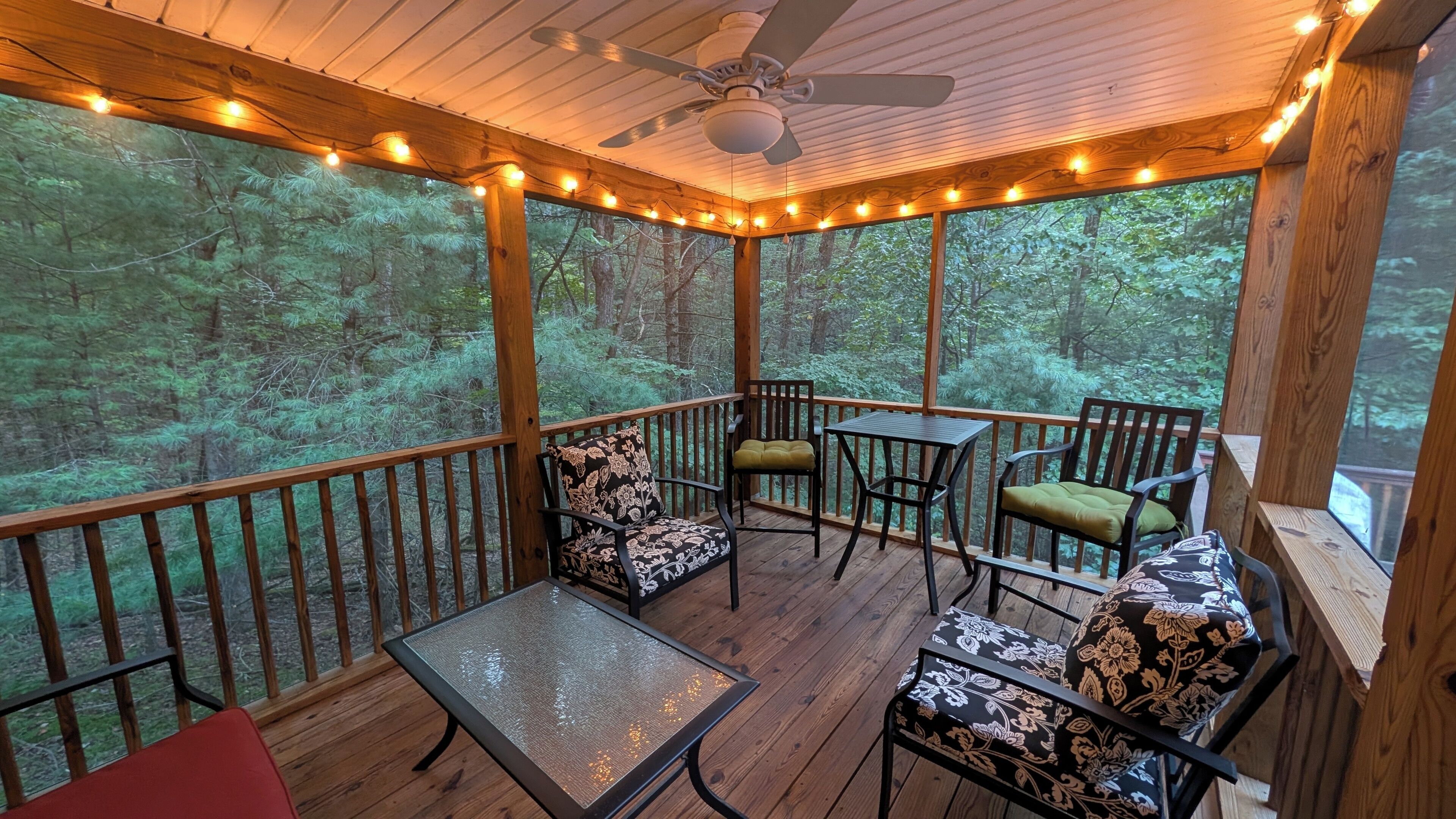 Une terrasse extérieure couverte, dotée de rampes en bois, d’un ventilateur de plafond, de guirlandes lumineuses et de sièges agrémentés de coussins à motifs.