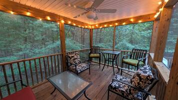 Une terrasse extérieure couverte, dotée de rampes en bois, d’un ventilateur de plafond, de guirlandes lumineuses et de sièges agrémentés de coussins à motifs.