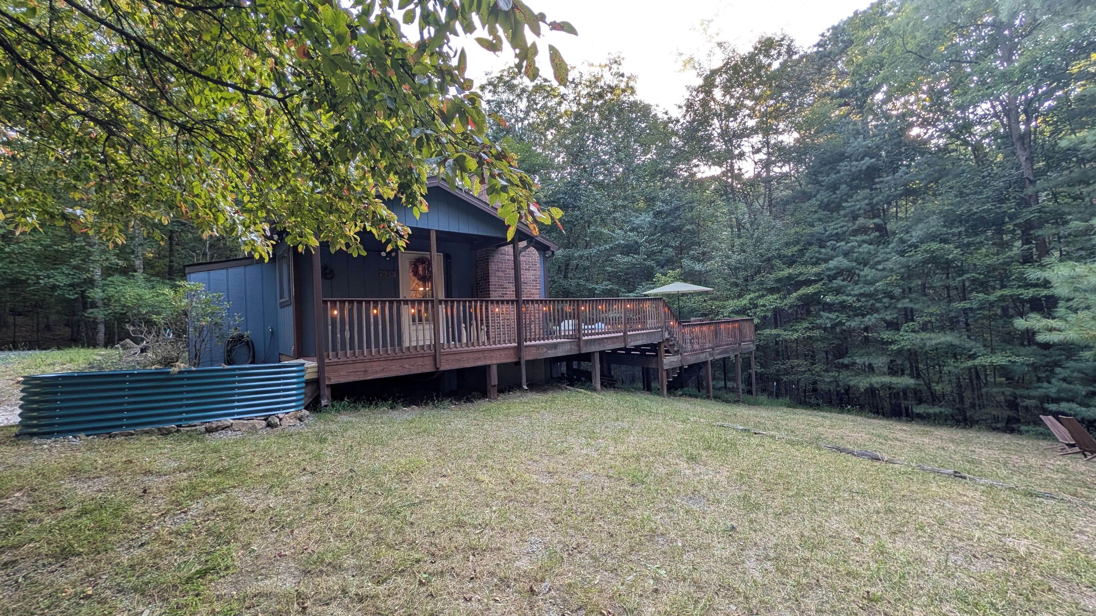 Une cabane en bois dotée d’une terrasse et d’un porche couvert, entourée d’une zone boisée.