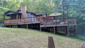 A rustic cabin with a brick chimney, wooden deck, and outdoor seating area.