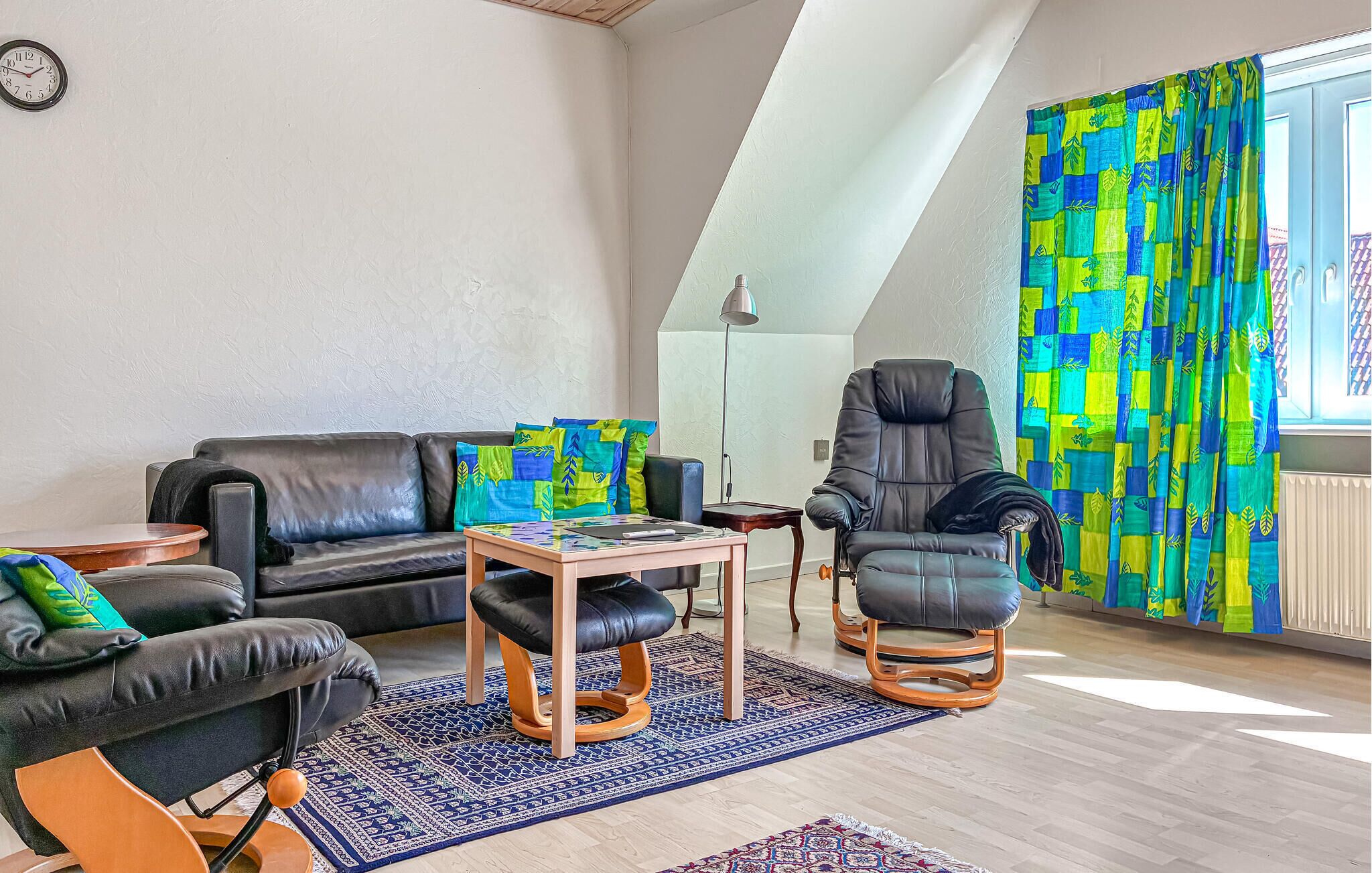 Una sala moderna con un sofá de cuero negro, un sillón de cuero negro, una mesa de centro de madera y un tapete estampado.