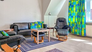 A modern living room with a black leather sofa, a black leather armchair, a wooden coffee table, and a patterned rug. - Cozy apartment in Højer with WiFi (Højer)
