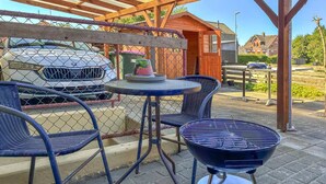 A patio area with a round table and two chairs, a barbecue grill, and a car parked behind a chain-link fence. - Cozy apartment in Højer with WiFi (Højer)