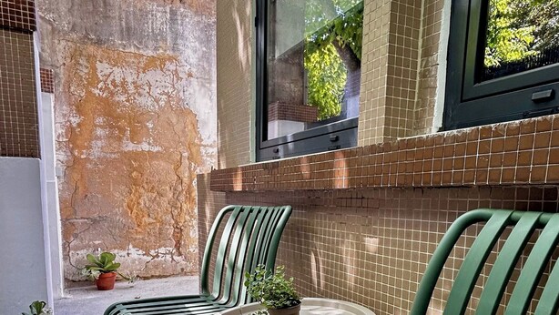 An outdoor seating area with green metal chairs and a small round table, featuring a view through a window to a brick wall and greenery. - Cobalt - Casa do Parque (Aveiro)